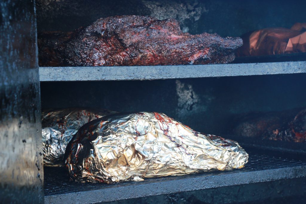 Unwrapped and foil-wrapped briskets at Camp Brisket